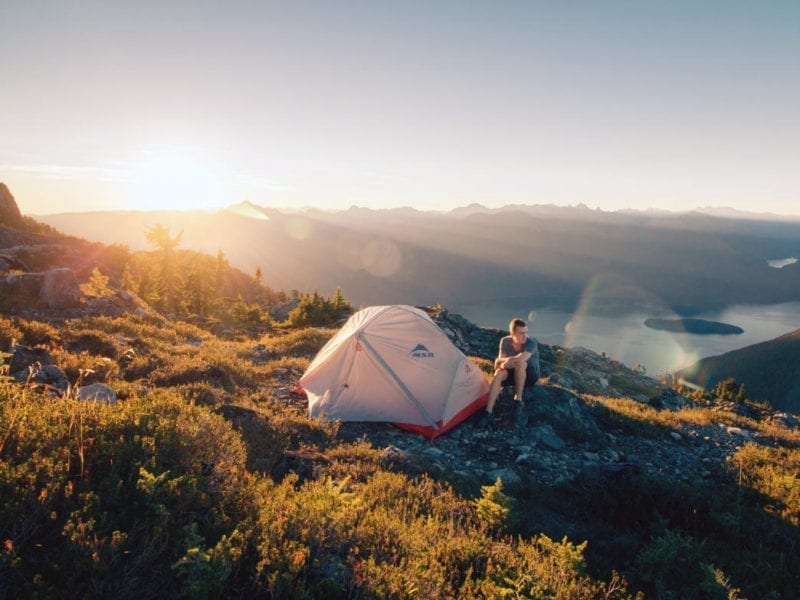 Man sitting by MSR tent in the hills over a lake