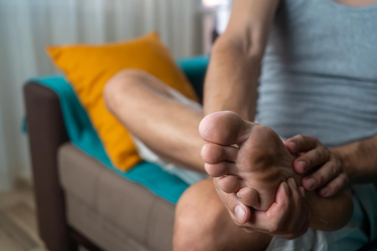 Pain in the foot, man holds hands to his feet, foot massage, cramp, muscular spasm, red accent on the foot, close-up